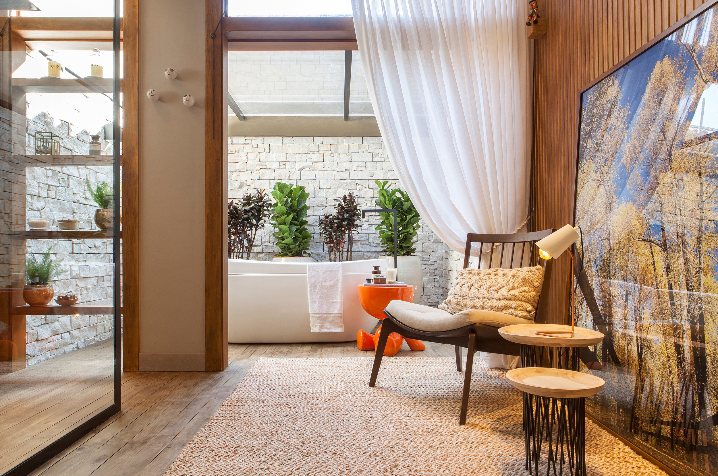 Sala de Banho do Casal - Elaine Queçada e Juliana Brigagão. Materiais naturais e a diversidade de plantas levam a natureza para dentro de casa, um refúgio relaxante com conforto e bem-estar. A banheira de imersão é a protagonista do ambiente, que é totalmente integrado pelo uso contínuo do deck de madeira. O pergolado de vidro valoriza a luz natural no espaço.