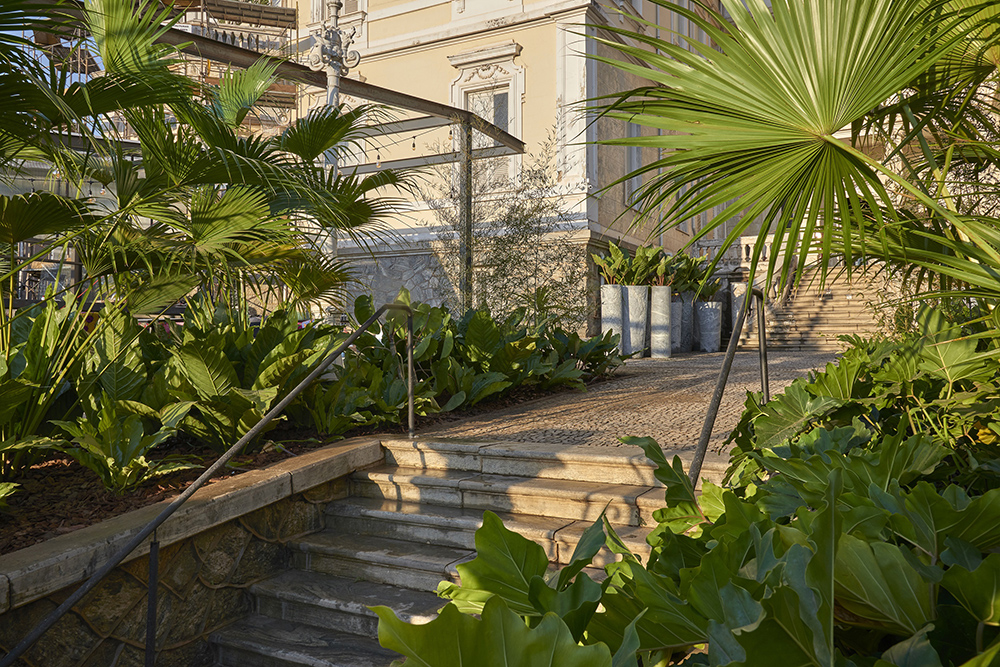 Jardim de entrada e do Pavilhão Nuvem - Felipe Fontes. Desenvolvido ora em canteiros geométricos existentes no casarão, ora em vasos de chapa metálica, o jardim potencializa a presença da vegetação e integra espaços de forma orgânica. As folhagens tropicais e a riqueza de espécies - essencialmente verdes - dão vida à composição imponente de texturas e volumetrias.