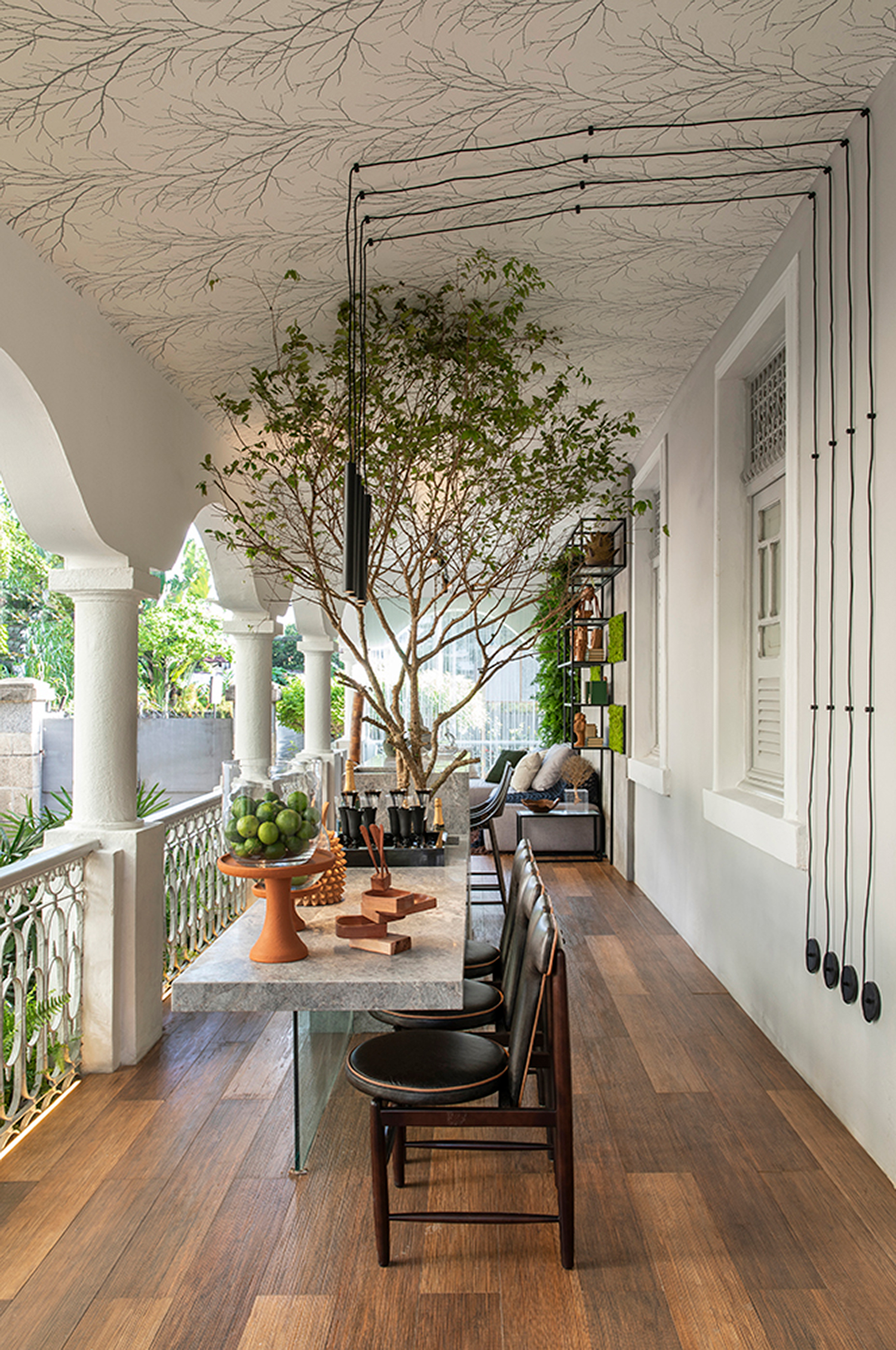 Varanda do Jantar - Igor Cabral. Elementos pernambucanos dialogam com móveis de design brasileiro, no espaço que preserva detalhes arquitetônicos do casarão de 1930. A extensão do ambiente permitiu criar um estar, área de relaxamento e o ambiente para preparar drinks e snacks, com a bancada em pedra e vidro voltada ao jardim. Outro destaque é a presença da jabuticabeira.