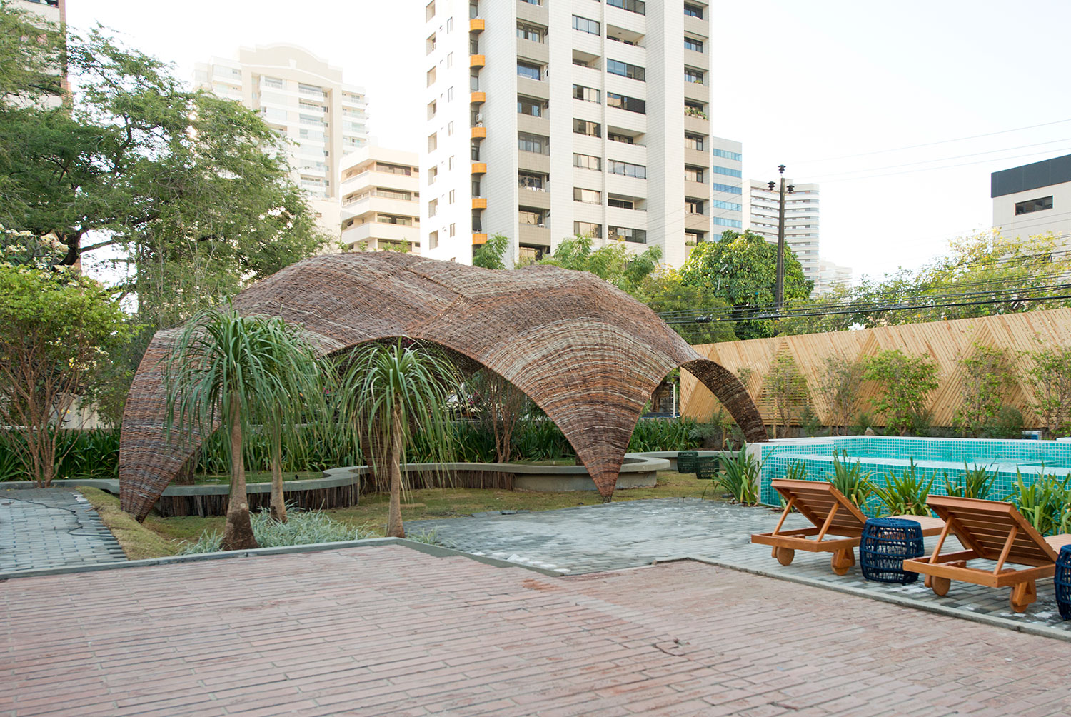 CASACOR Ceará 2018. Jardim com Piscina - Arthur Bonavides, Bruno Frota e Carlos Zaranzza. Tendo como ponto de partida a espiritualidade, o ambiente tem como objetivo proporcionar uma fuga do estresse e da correria do dia a dia. Para tal escape, o trio de profissionais explora a vegetação e cria um espaço dedicado à meditação e à busca pela paz interior. Um dos destaques é o uso de elementos que fazem referência, de forma sucinta, aos quatro elementos - água, fogo, terra e ar. Outro diferencial é a oca, feita de maneira conceitual com materiais como bambu, localizada em meio à natureza de um jardim verde e com a intenção de proporcionar conforto, comodidade e bem-estar.