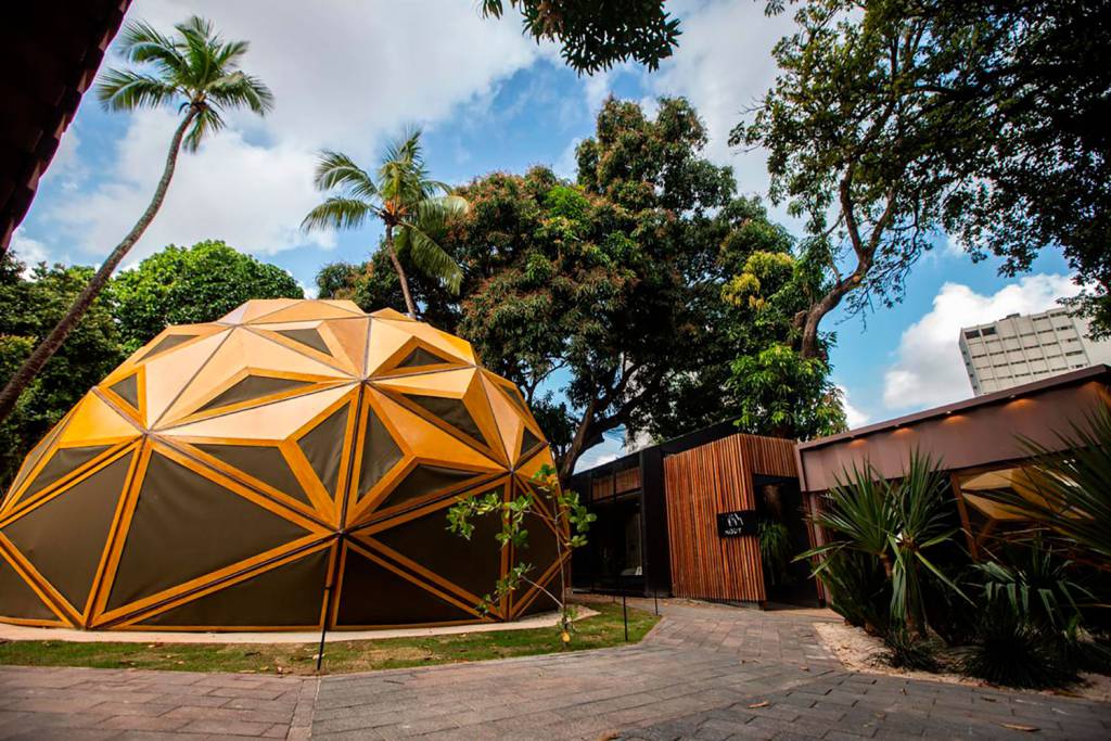 Pernambuco 2018. Arena Arbor - Paulo Carvalho. A Arena possui um conceito vivo e vai além de apenas um espaço assinado: transforma-se em instalação arquitetônica e é um convite à experimentação e uso concreto do local. O ambiente é inspirado em uma árvore, representante do símbolo da vida, levando em consideração todas as suas faces: raiz, tronco, copa, flor e fruto. A estrutura desmontável agora passará a fazer parte do Jardim Botânico do Recife.