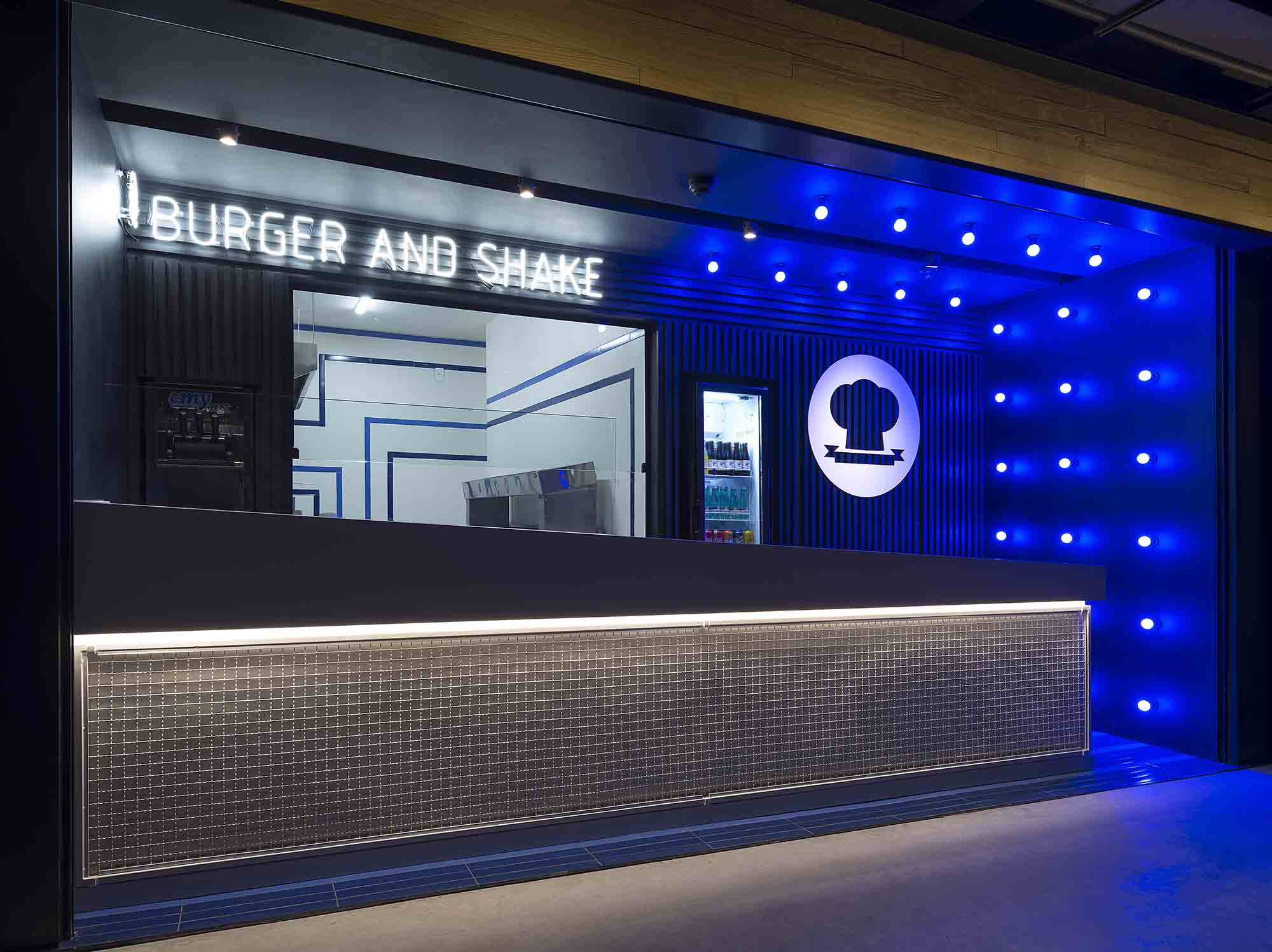 Burger Dream - 3P Studio. Com uma fachada única, o projeto enaltece as linhas retas, o gradil, o P&B e a cor azul da primeira sede do restaurante. Painéis ripados na cor preta emolduram e destacam a grande vitrine para a cozinha, na qual o movimento das linhas azuis quebram a formalidade dos volumes brancos. Repare que o grande balcão em Silestone foi instalado na diagonal para, mais uma vez, criar movimento e refletir já no primeiro momento o dinamismo da operação.