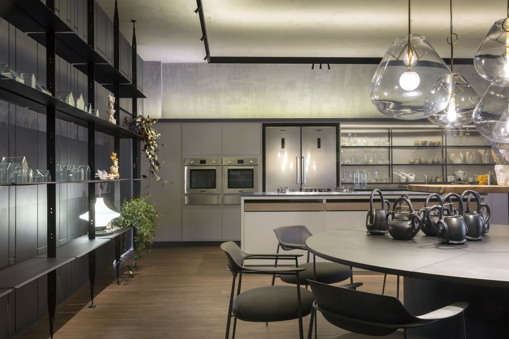 Cozinha DECA - Walléria Teixeira. São 100 m² em que sala de estar e espaço gourmet ficam ao lado do verde das plantas internas. Funcional, aplica em uma linguagem moderna um espaço ideal para receber, conversar e passar o tempo. O piso de madeira contrapõe o revestimento cinza das paredes, que dialoga com as cubas de aço inox e os revestimentos em linho, couro e pedras naturais.