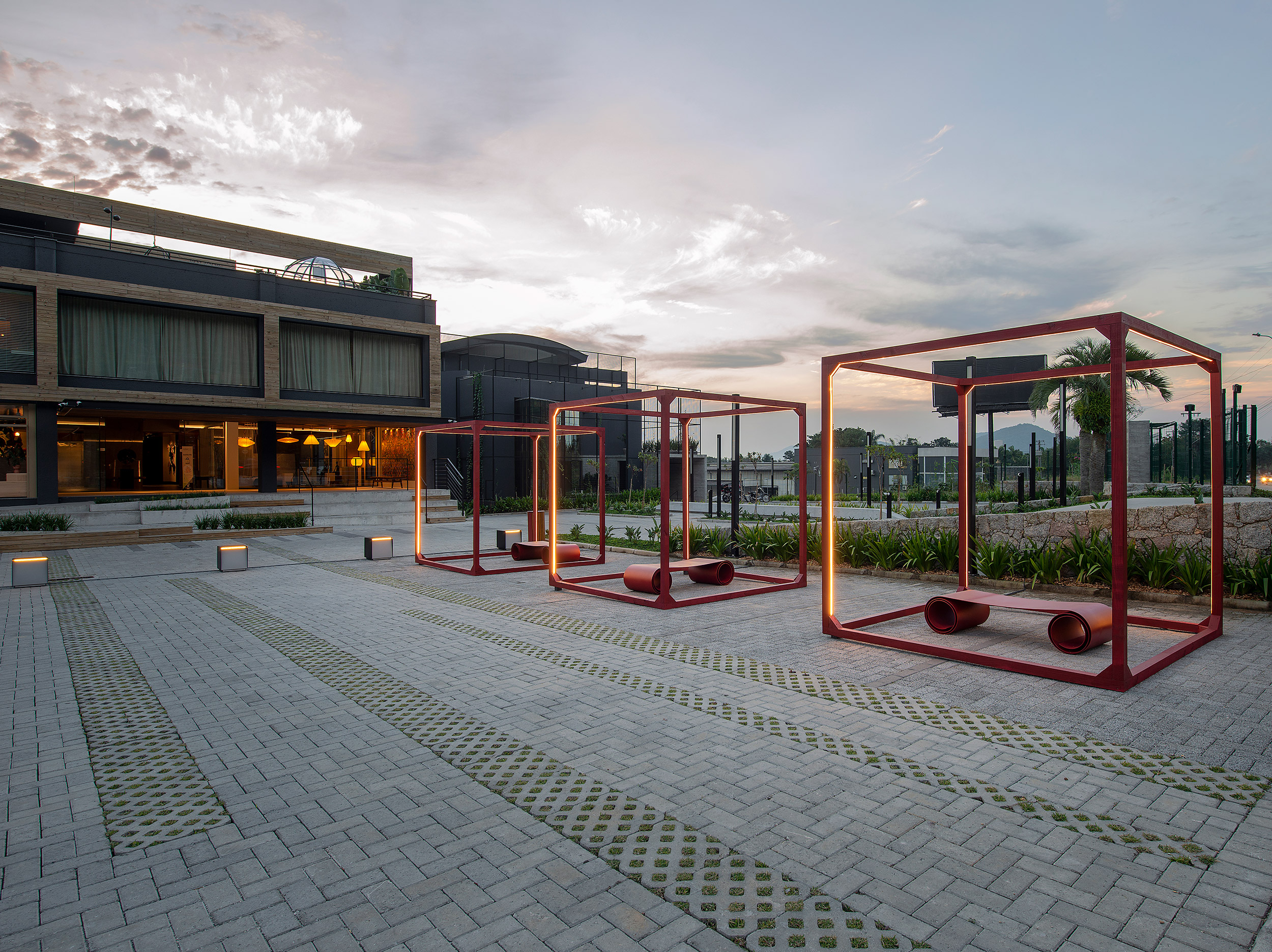 Quem cria nasce todo dia - Ana Trevisan | Paisagismo + Arquitetura. O estacionamento de 270 m² foi transformado em praça para recepcionar os visitantes e a instalação dos cubos faz uma analogia com o momento atual, no qual precisamos nos refugiar em nossas casas. Os bancos sinuosos são peças assinadas pelo arquiteto Jaime Lerner e nos convida a uma pausa para a reflexão. À noite o jardim ganha iluminação pontual e cênica.