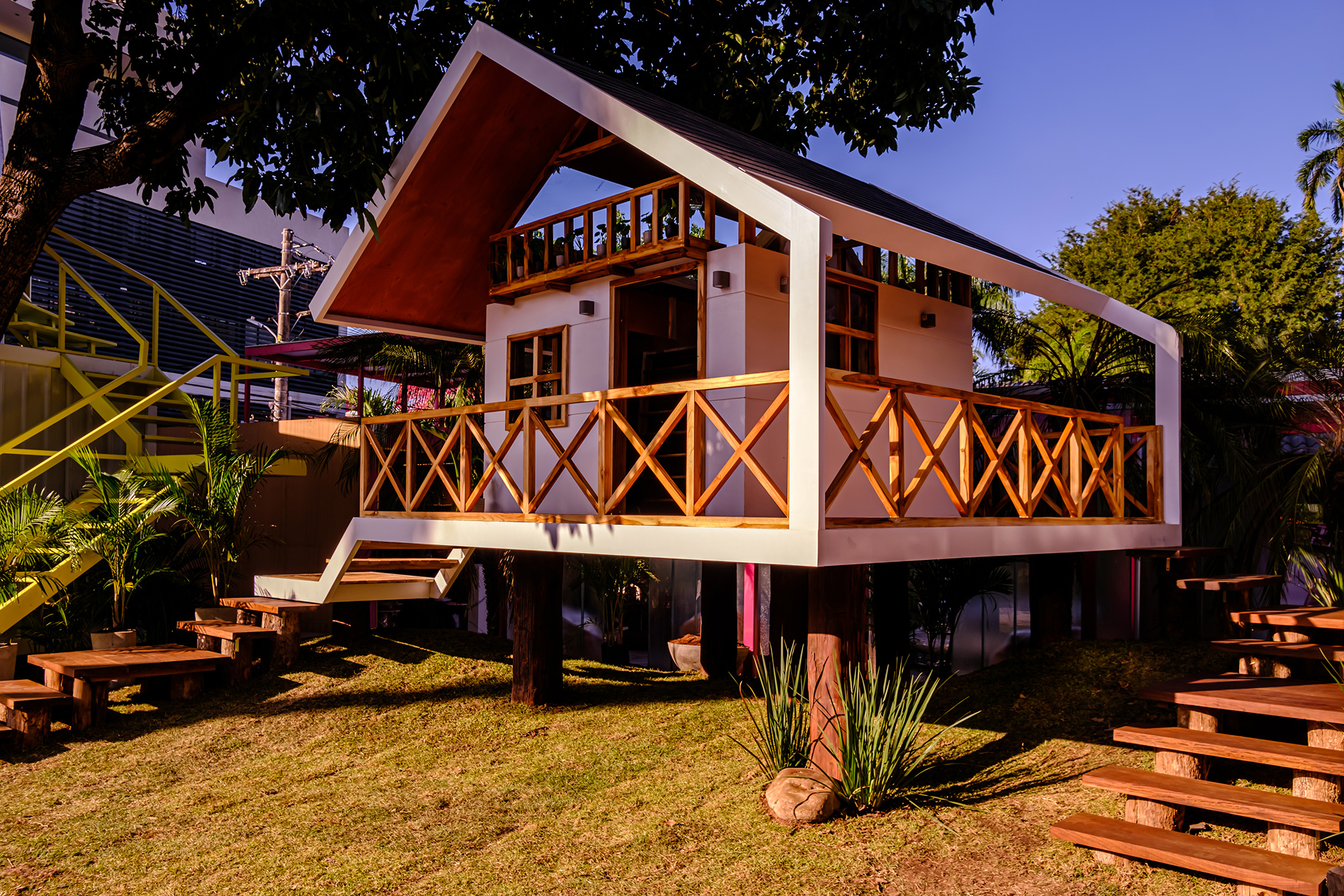 Diana Canedo - La Casa del Árbol. Diana Canedo aproveitou um antigo abacateiro para construir a The Tree House. Mas, ao contrário daquelas construções para crianças, esta pode ser visitada por adultos para desfrutarem de suas atividades com eles. A estrutura de madeira de 15 m2 é sustentada por troncos de cuchi como estacas. A decoração do espaço interior é feita por artesãos, utilizando fios Chiquitano com pigmentos neutros, que harmonizam com o calor dos acabamentos da madeira natural. Da cama do segundo andar, através de uma clarabóia, você pode ver os galhos da árvore iluminados do lado de fora. Mas, sem dúvida, o mais interessante é sua adaptação ao modo de jogo das crianças de hoje, através de seu sistema de automação residencial: a voz é suficiente para controlar a luz, ativar e desativar a música e a televisão.