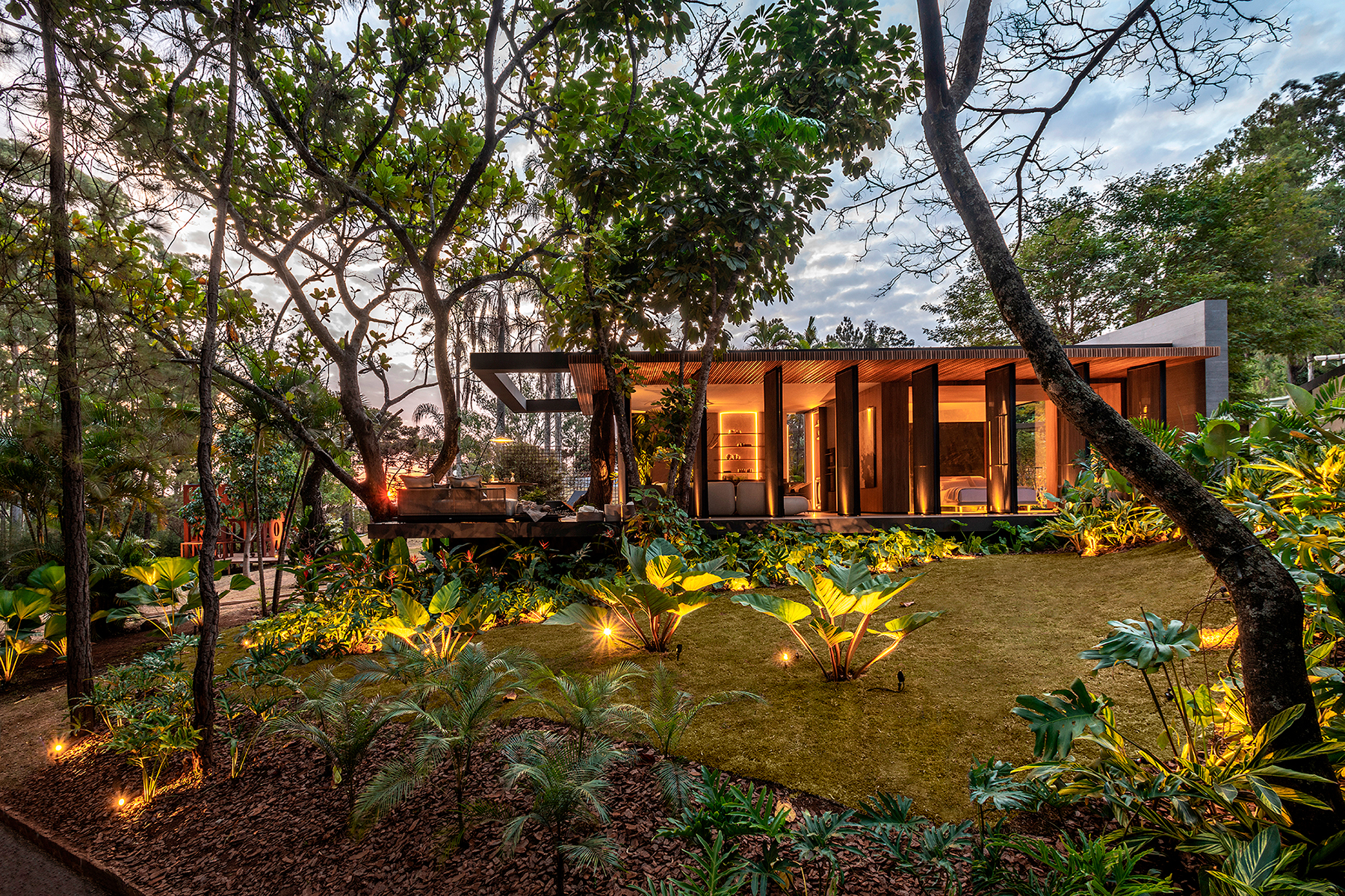 Jardim Fleury Paisagismo - Origens. Criado para abraçar e envolver a arquitetura, este jardim traz elementos que provocam sensações proporcionadas pelos aromas, pelo tato e experimentação, e também pelo resgate de memórias afetivas. Une vegetais tropicais a espécies típicas dos quintais mineiros, como a jabuticabeira, além de plantas esculturais. Entre vários tons de verde e uma volumetria bem trabalhada, o cordyline traz pontos magenta.