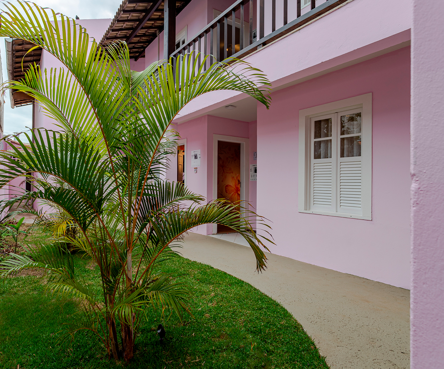 Joilson Barbora, Luis Damarant, Tânia e Paula Facchinetti - Casa de Saúde Solange Fraga (Paisagismo). No paisagismo assinado pelo quarteto, a grama no corredor lateral da casa traz um clima de natureza para a área externa que ganhou plantas ao redor e uma palmeira central que dialoga com os desenhos lúdicos das paredes no entorno do jardim.