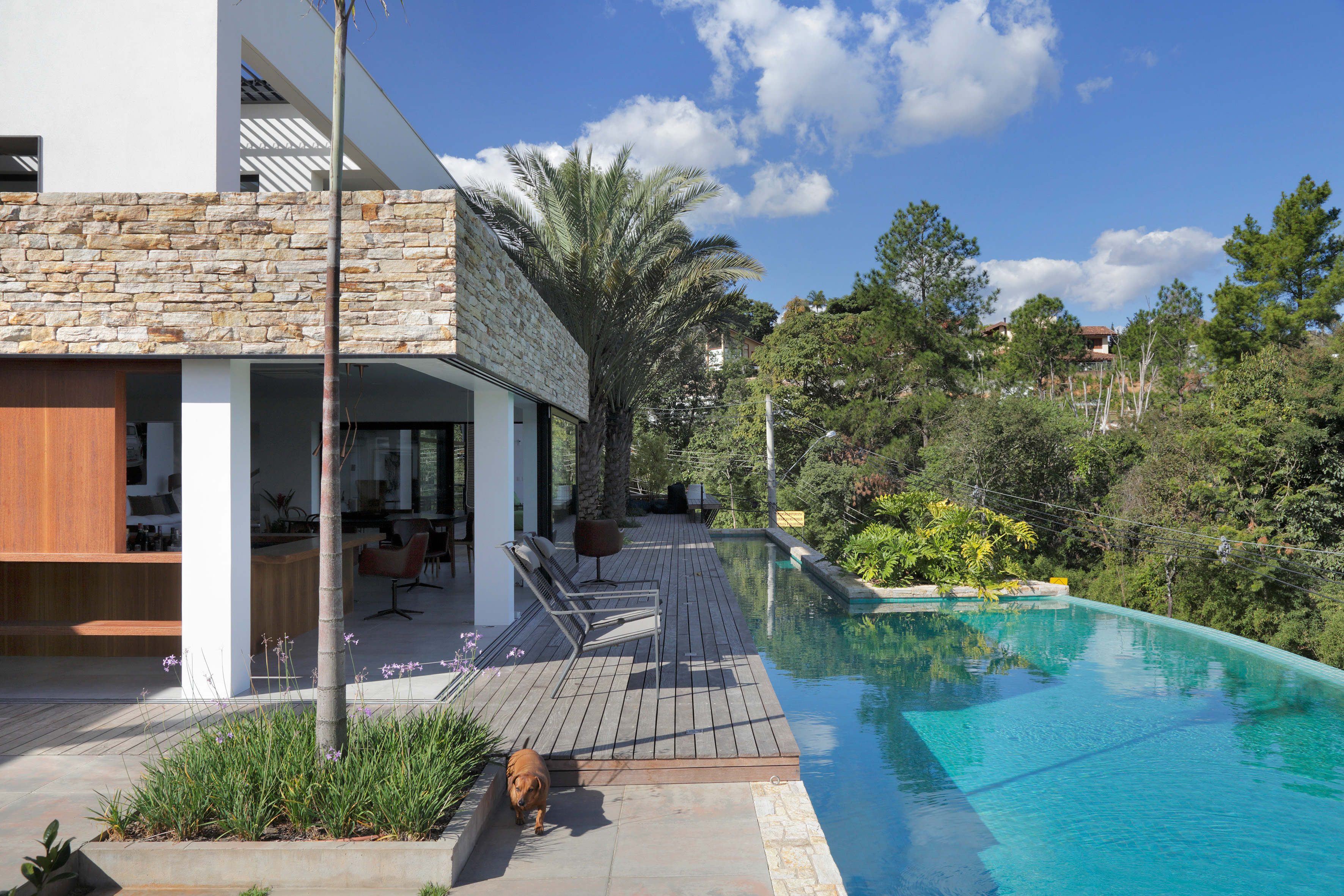 Parede pedra integra interno externo casa de campo. Otto Felix arquitetura decoração paisagismo jardim piscina deque madeira cadeira varanda