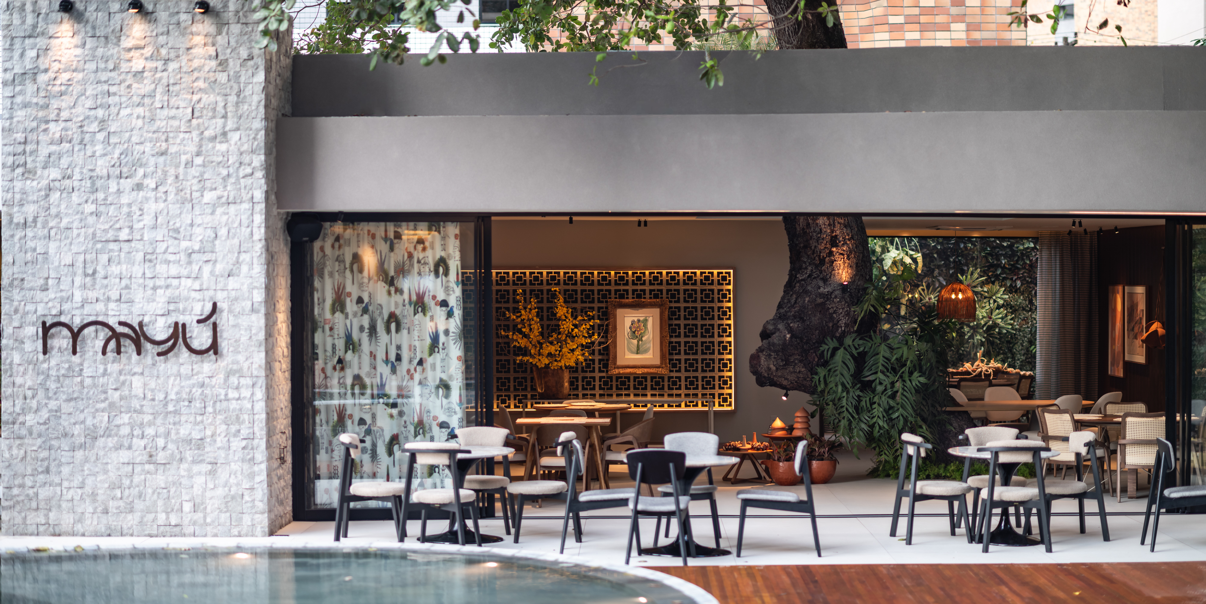 Neide Barbosa e Denise Bessa - Restaurante MAYU. O restaurante propõe uma atmosfera contemporânea com elementos da arquitetura brasileira, como cobogós, concreto e luz natural, resgatando a cultura cearense através de materiais como barro, palha e madeira. A varanda é um destaque para a transição do ambiente externo para o interno, O objetivo do projeto foi criar um ambiente que promova o bem-estar, conectando-se com a natureza e as raízes culturais, proporcionando um espaço para momentos de descontração e alegria.