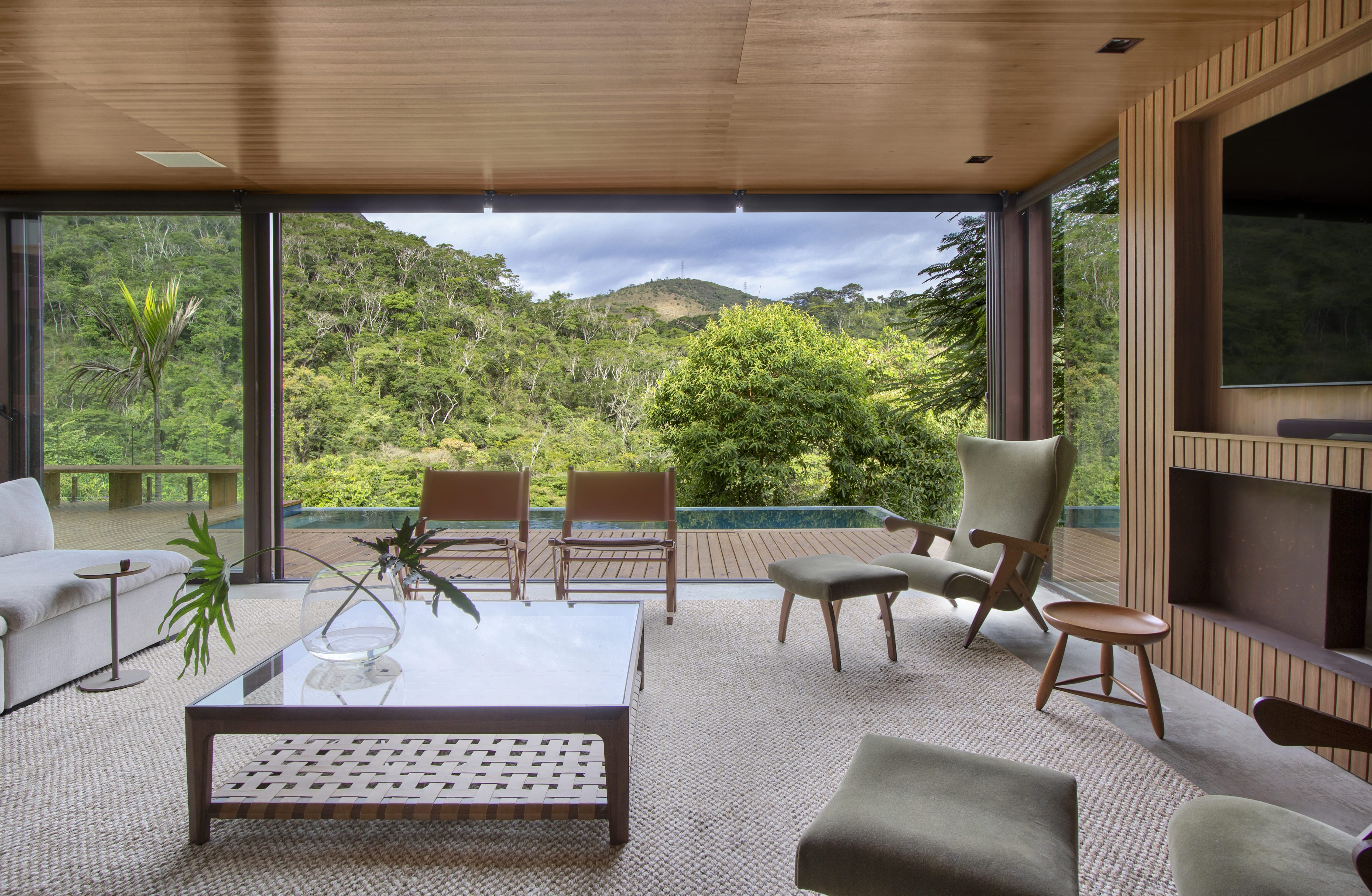 Casa repleta de materiais naturais vira refúgio com vista para a Serra. Projeto de Diego Raposo e Manuela Simas. Na foto, sala com vista para o deque com piscina e para a serra.